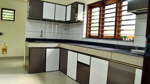 Una cocina con armarios blancos y oscuros, una encimera negra y una ventana con persianas de madera.