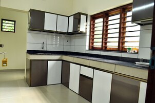 Una cocina con armarios blancos y oscuros, una encimera negra y una ventana con persianas de madera.