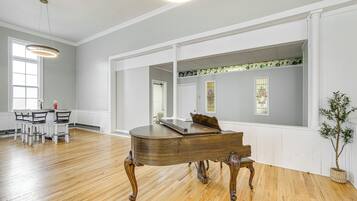 Una habitación amplia con un piano de cola, suelo de madera y ventanas grandes.