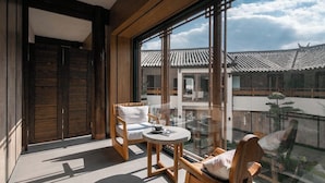 A balcony with two wooden chairs and a small table, overlooking a traditional building with tiled roofs. - Lijiang Garden vacation PuZhi hotel (Lijiang)
