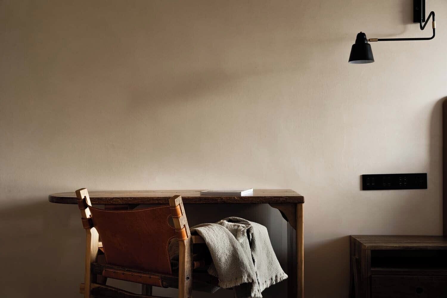 A small, cozy room with a wooden desk, a chair, a lamp, and a nightstand.
