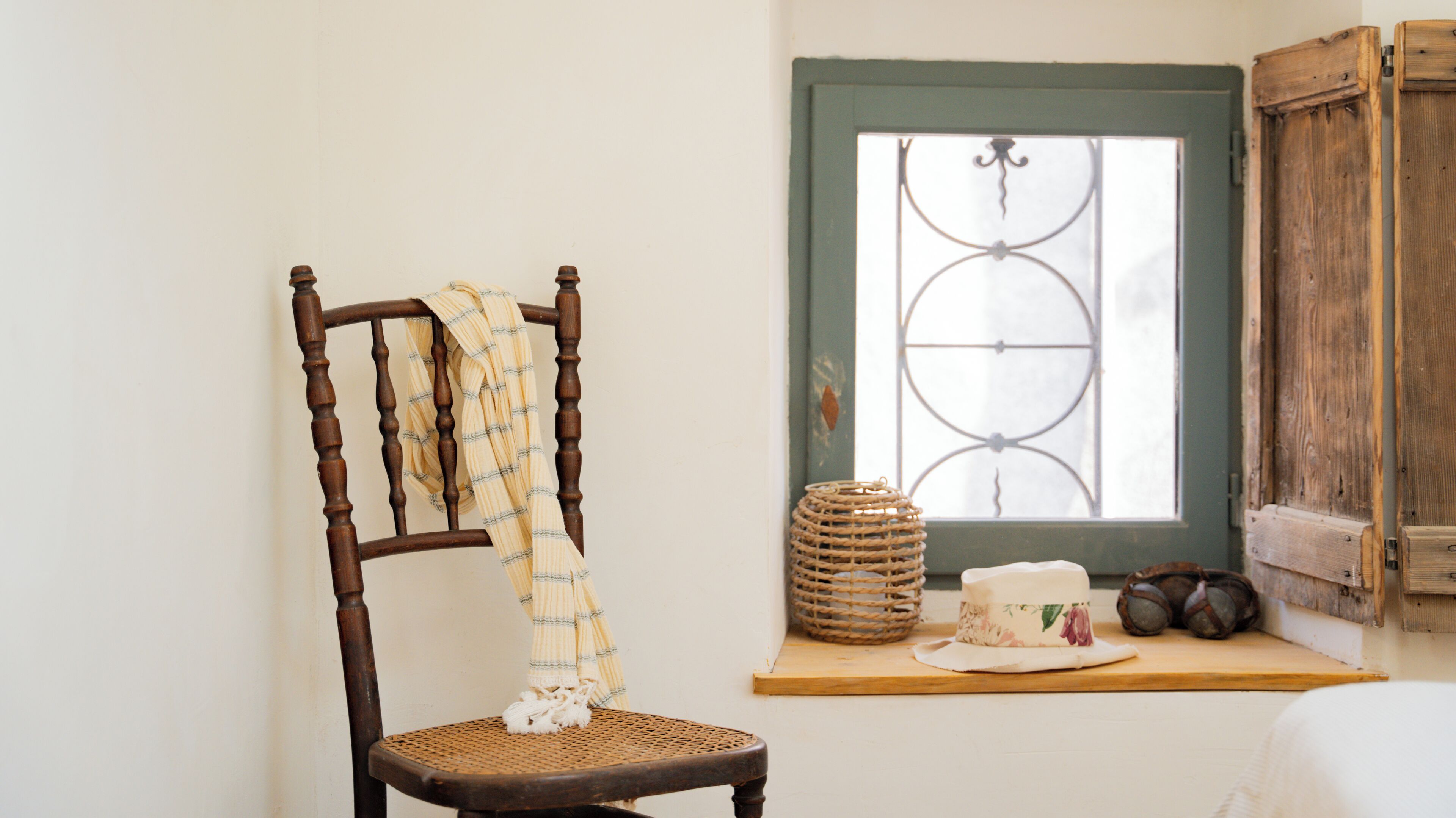 A wooden chair with a plaid blanket, a wicker basket, and a small table with a decorative item and a hat.