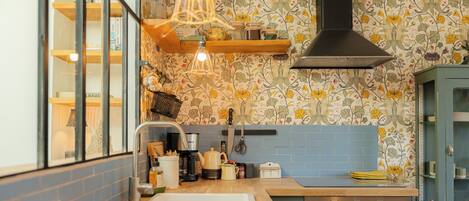 A kitchen with a wooden countertop, a sink, a stove, and a backsplash with floral wallpaper.