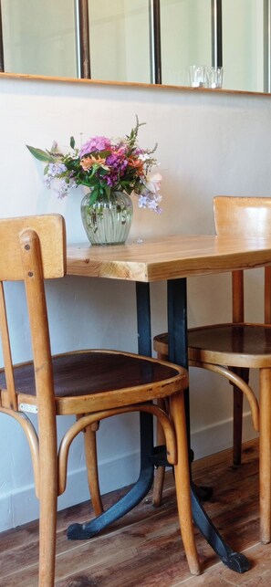 A wooden table with a vase of flowers, two wooden chairs, and a mirror on the wall.
