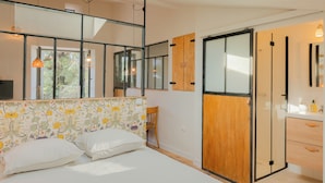 A bedroom with a bed, a wooden wardrobe, a mirror, and a window with a view of greenery. - Charming studio in lovely Les Vans, National Park Monts d'Ardèche, river nearby. (Les Vans)