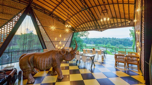A restaurant with a checkered floor, a large rhinoceros statue, and tables and chairs. - Oxy Resort Chiangrai (Mae Chan)