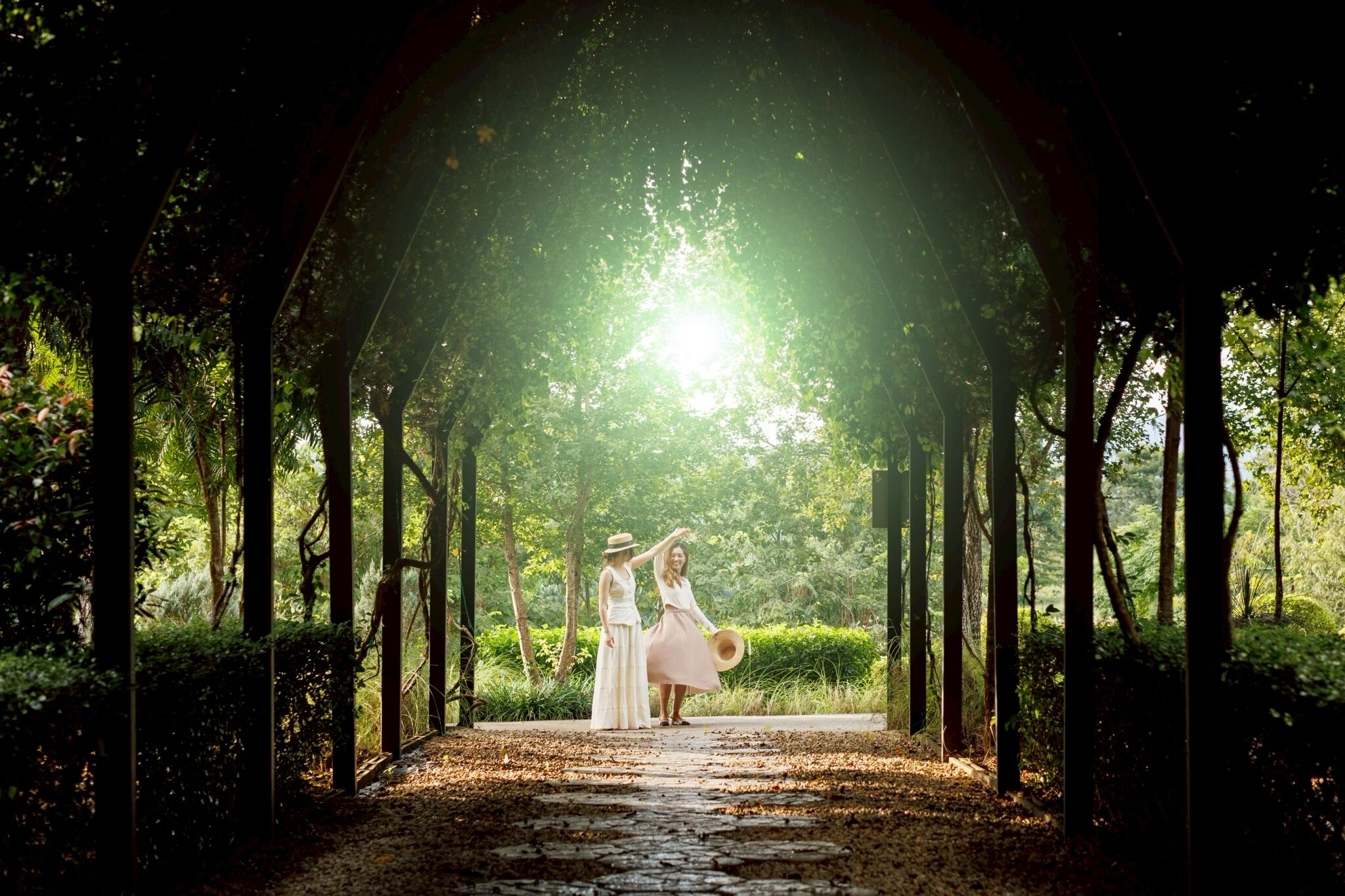 A covered pathway in a lush garden with a wooden structure overhead.