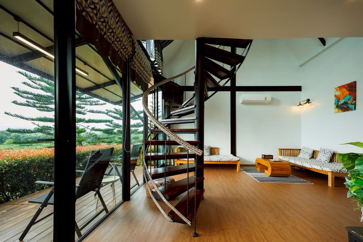 A modern interior with a spiral staircase, wooden flooring, a sofa, and a view of greenery outside.