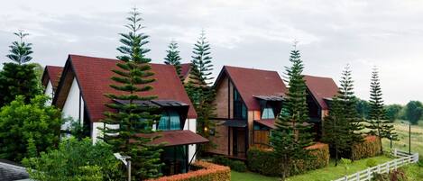 A row of modern houses with red roofs, surrounded by lush greenery and a white fence.