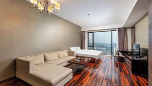 Una habitación de hotel moderna con sofá, cama, televisor y un amplio ventanal con vista a la ciudad.