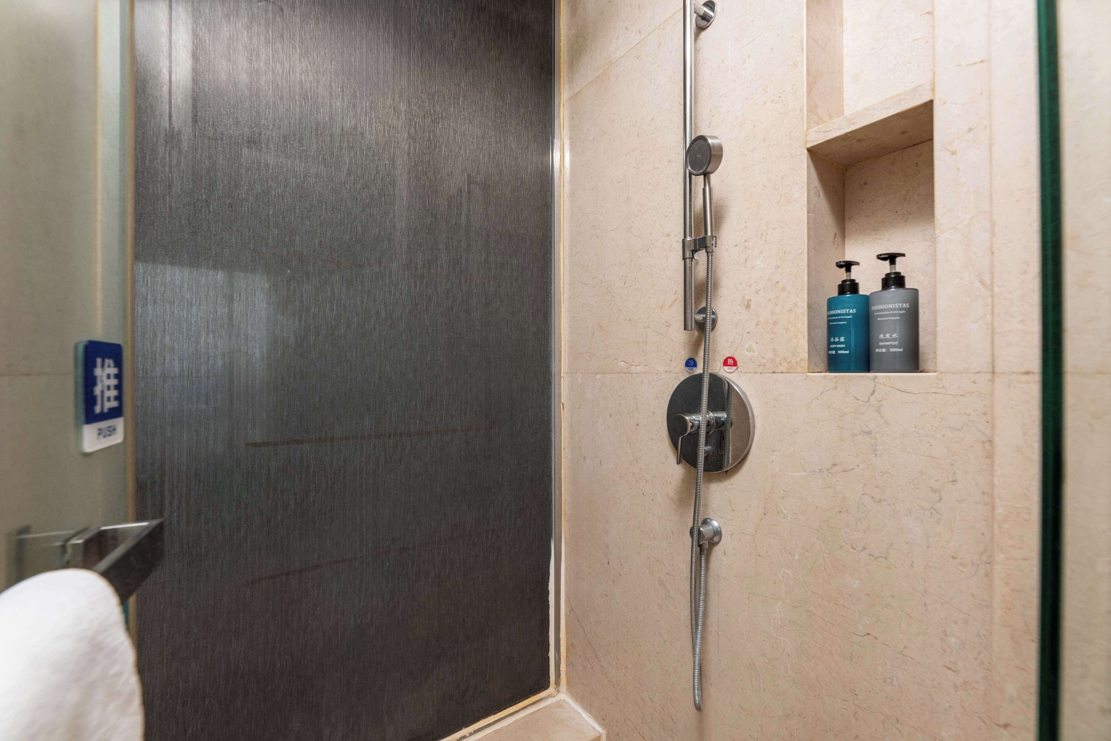 A bathroom with a shower, a towel rack, and a shelf with toiletries.