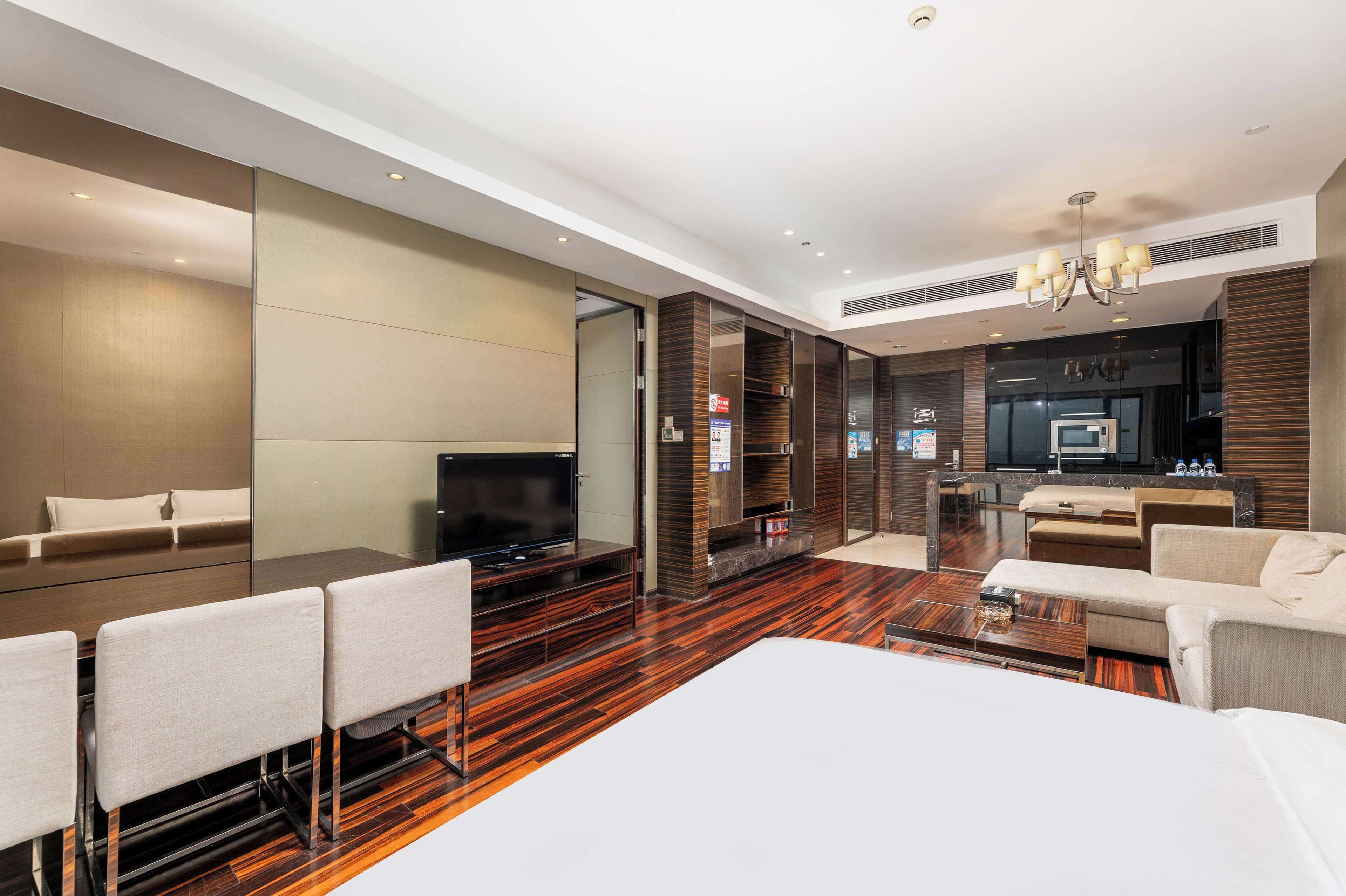 A modern hotel room with a large bed, a TV, a seating area with chairs, and a kitchenette.