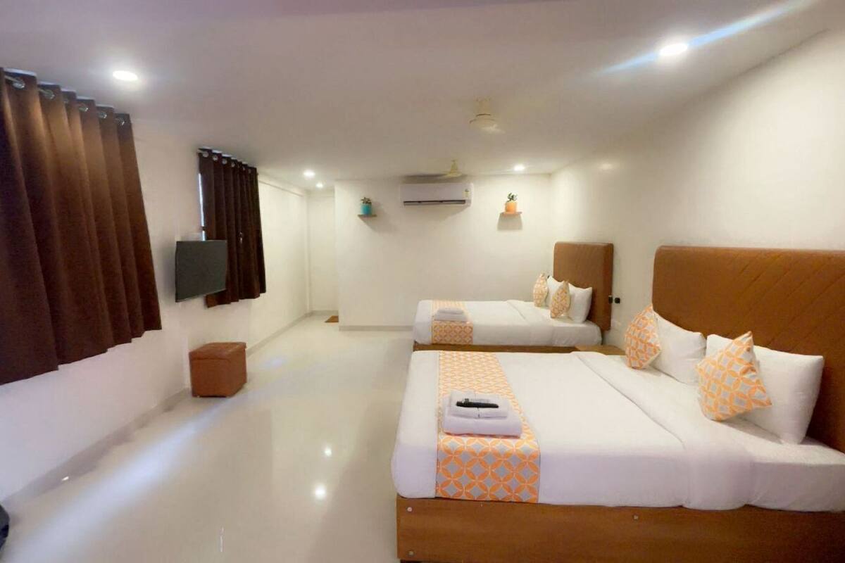 A hotel room with two beds, a flat-screen TV, an air conditioner, and a small ottoman.