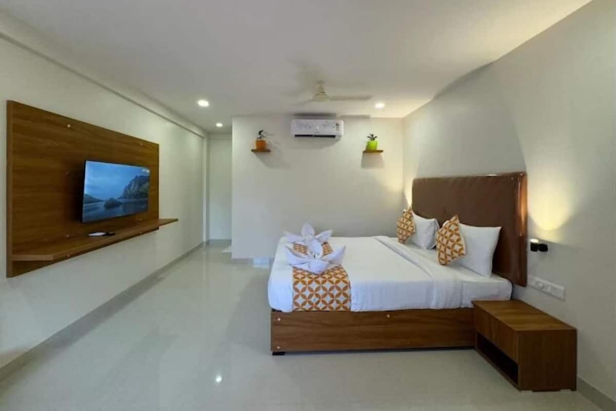 A modern hotel room with a large bed, a TV mounted on the wall, and a small bedside table.