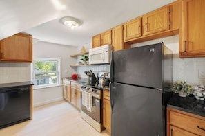 A modern kitchen with wooden cabinets, a black refrigerator, a stove, and a microwave. - Bright, Clean & Cozy Newly-Renovated 2BR! Welcome! (Ypsilanti)