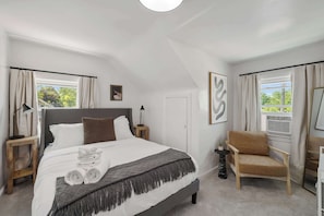 A modern bedroom with a large bed, a chair, and a small table. - Bright, Clean & Cozy Newly-Renovated 2BR! Welcome! (Ypsilanti)