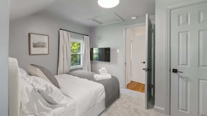 Un dormitorio con cama, una ventana con cortinas, un televisor de pantalla plana en la pared y una puerta que da a otra habitación.