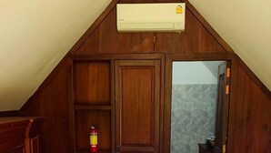 A bedroom with a large bed, wooden wardrobe, and an air conditioning unit on the sloped ceiling.