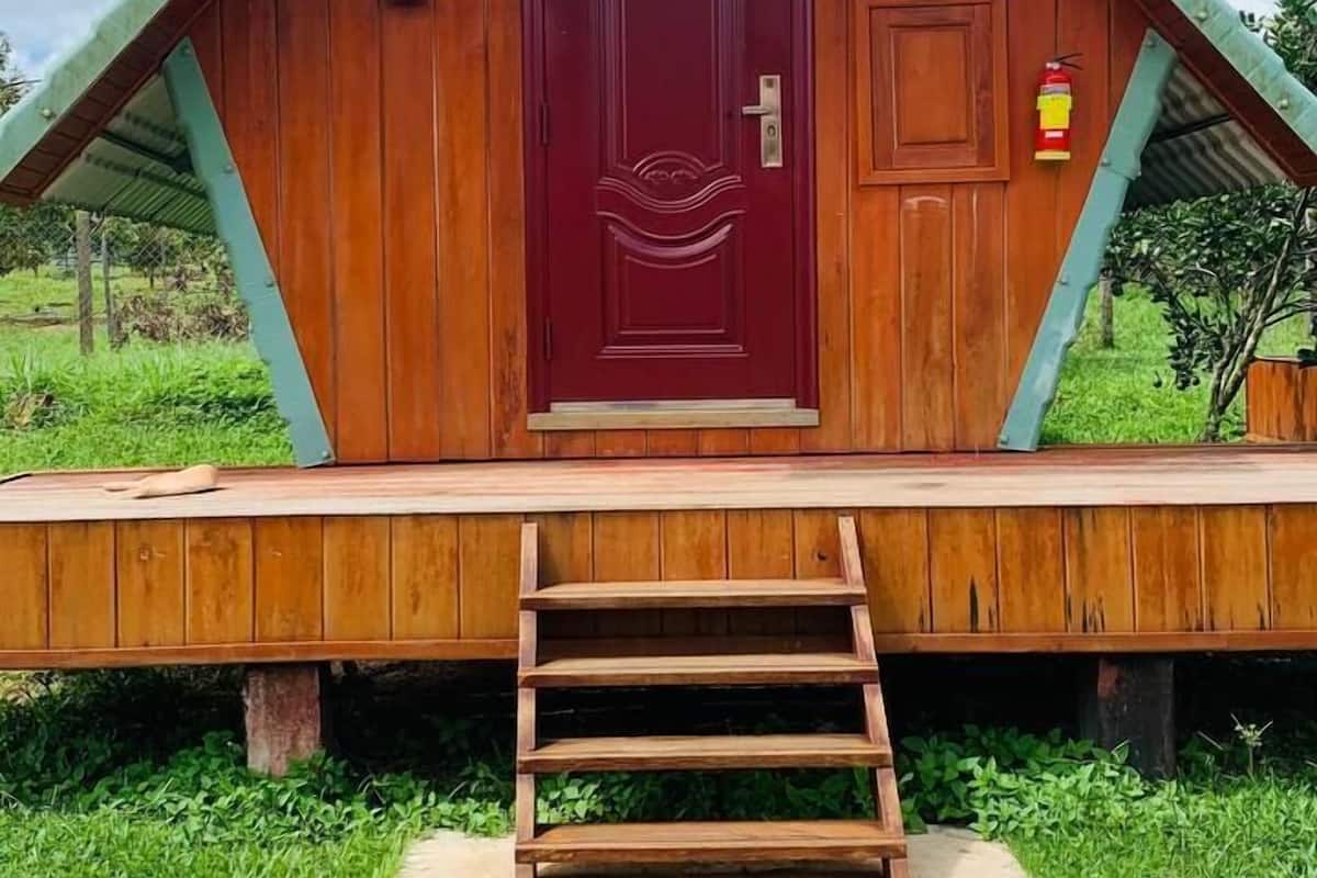 Un edificio de madera con una puerta roja, un ventanal pequeño y un extintor en la pared.