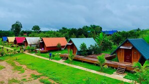 A row of colorful wooden cabins with a grassy path between them, surrounded by lush greenery.
