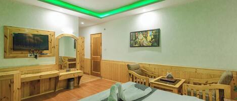 A hotel room with a bed, wooden furniture, a TV, a painting, and a ceiling fan.