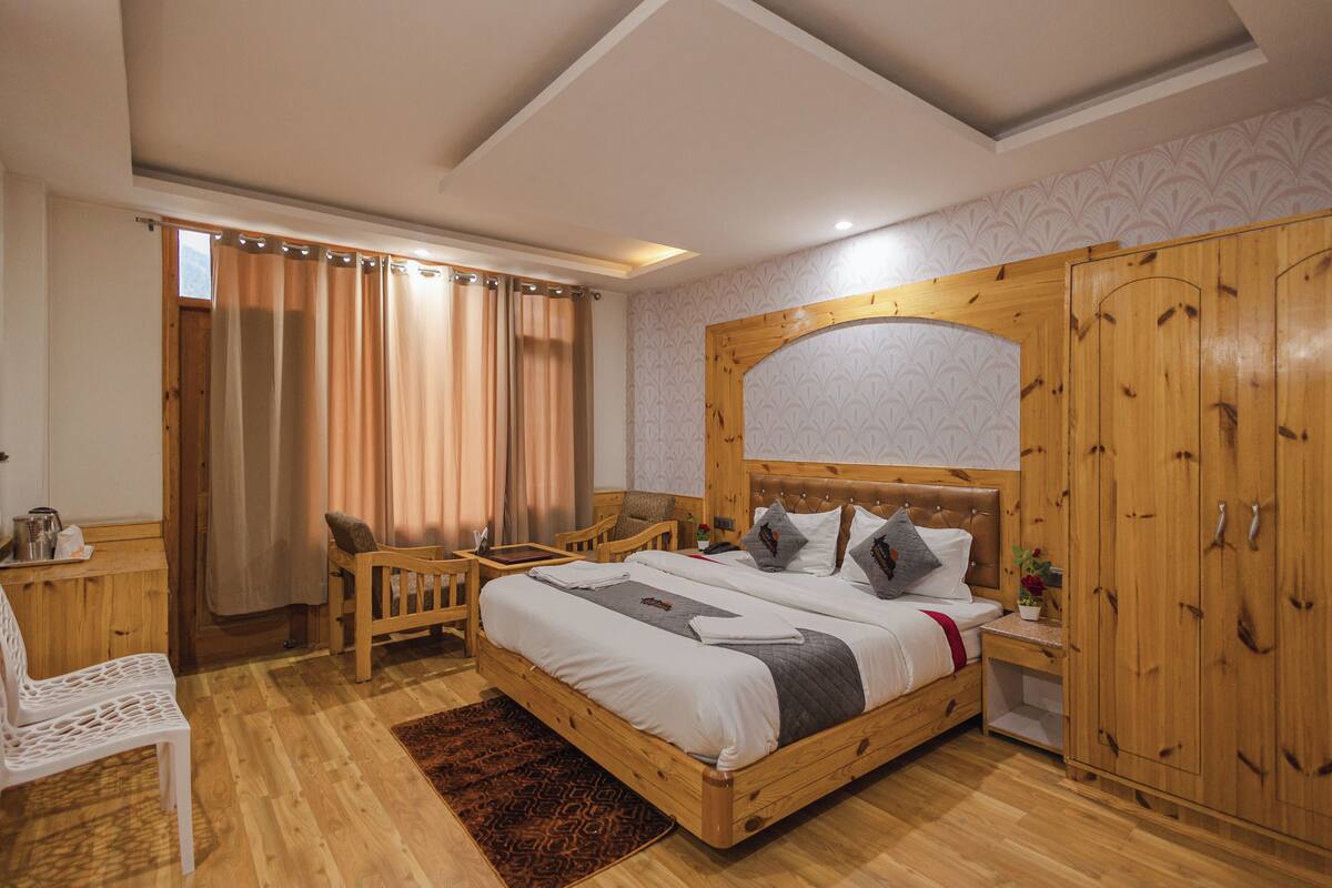 A bedroom with a wooden bed, a wooden wardrobe, a wooden chair, a wooden nightstand, and a window with curtains.