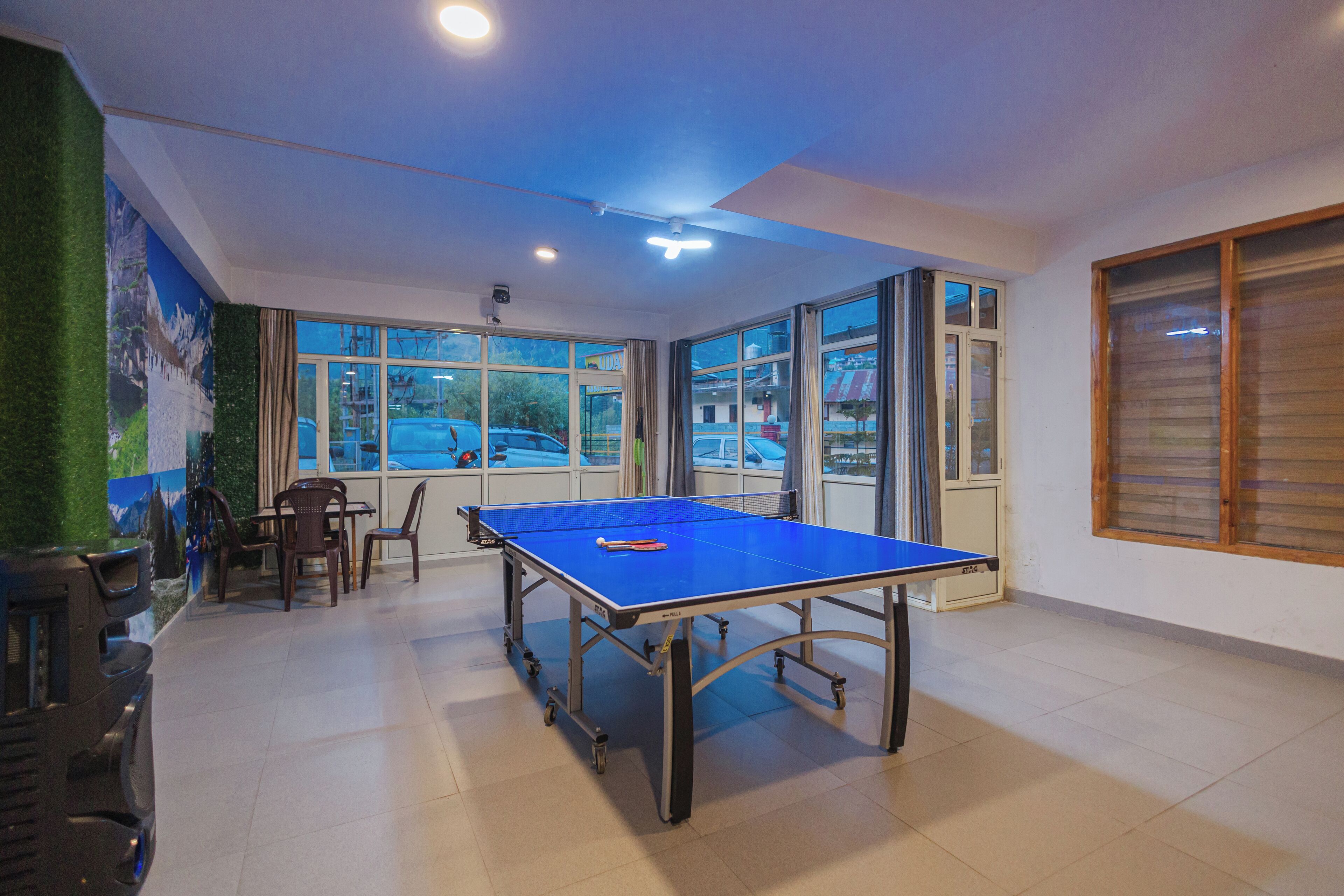 Une pièce avec une table de ping-pong, des chaises et de grandes fenêtres.