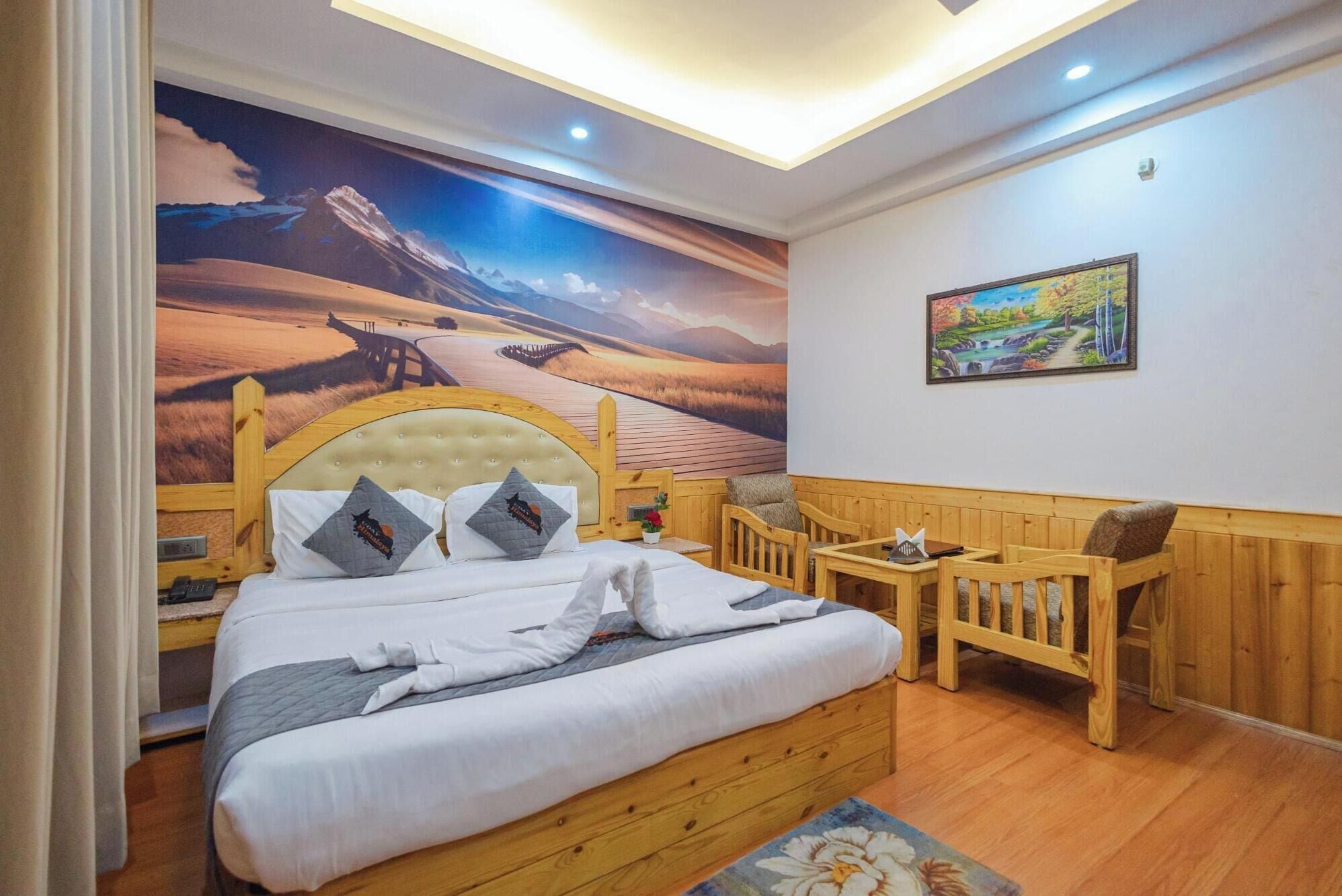 A bedroom with a large bed, wooden headboard, and a mural of a desert landscape. There is a small wooden table and two chairs.