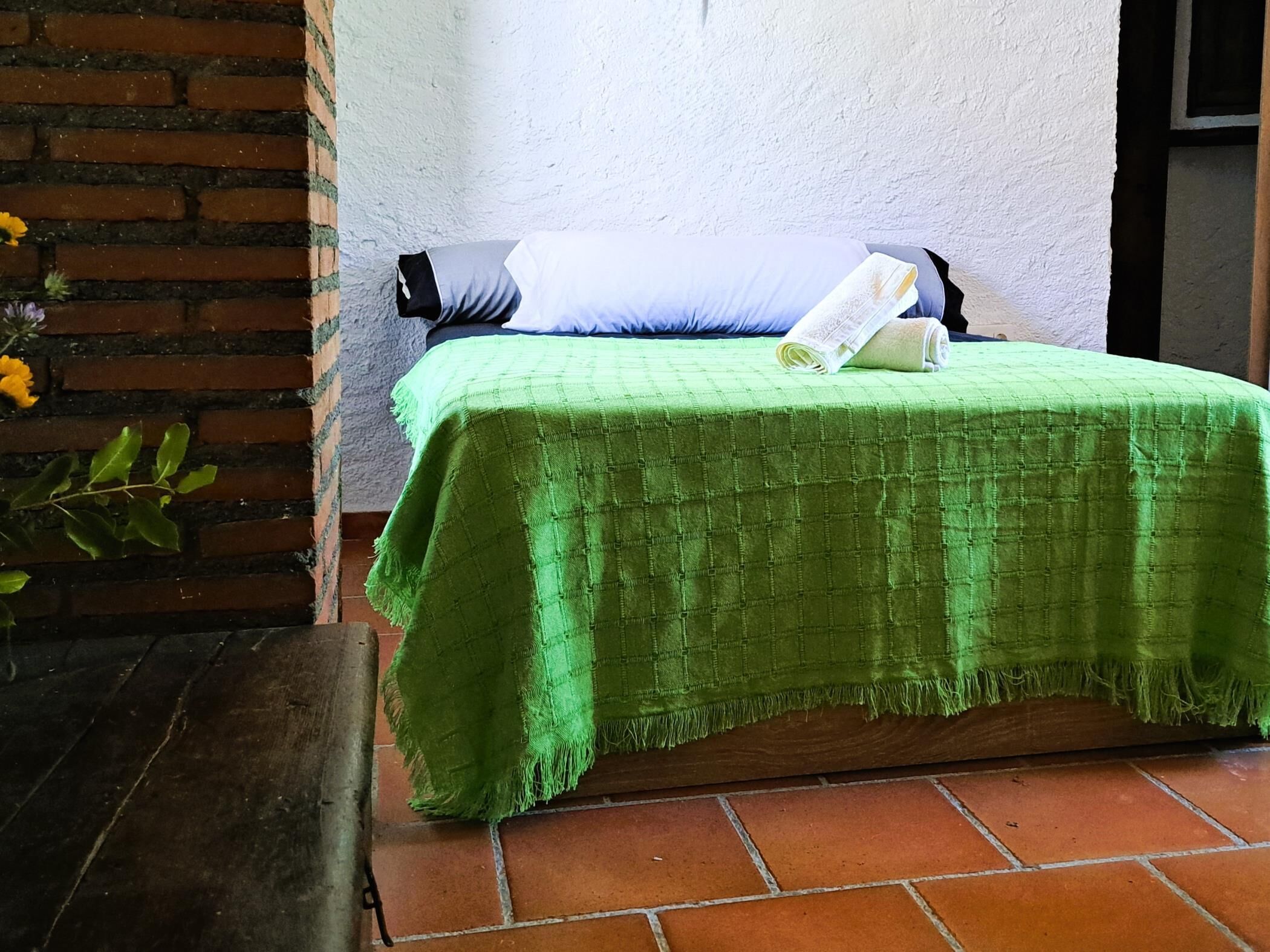 A room with a green bedspread, a pillow, and a folded newspaper on the bed.