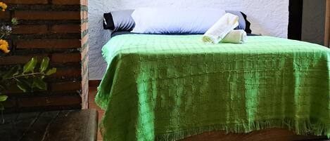 A room with a green bedspread, a pillow, and a folded newspaper on the bed.