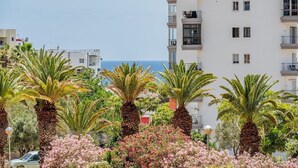 Um edifício com vários andares e varandas, rodeado por palmeiras e arbustos floridos.