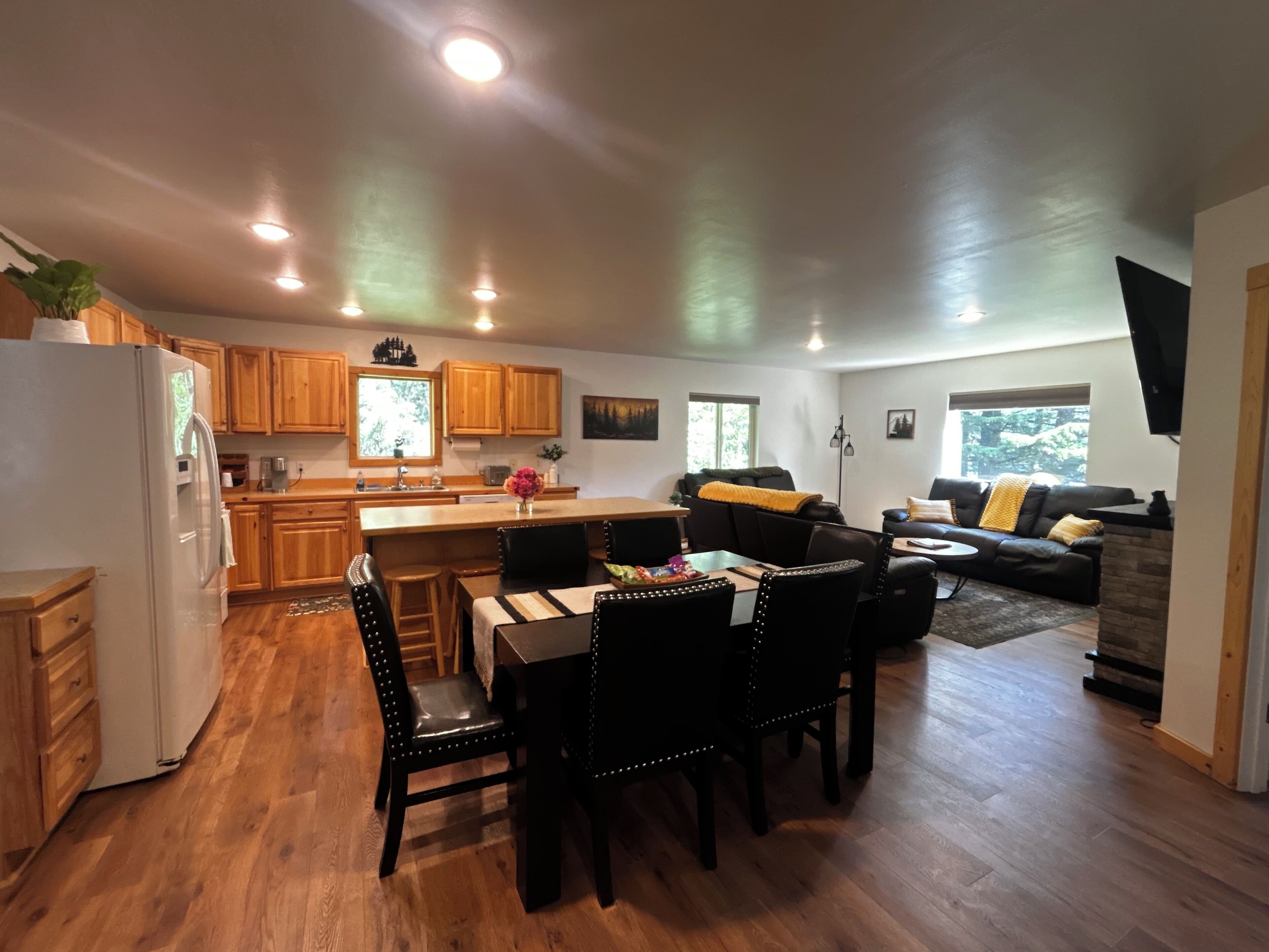 A spacious kitchen with wooden cabinets, a dining area with a table and chairs, and a living area with a sofa and a TV.