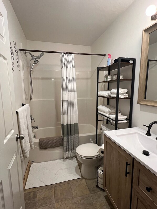 A bathroom with a shower, toilet, sink, and a towel rack.