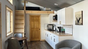 Une cuisine de taille réduite avec des meubles blancs, une porte en bois et un coin repas équipé de deux chaises.