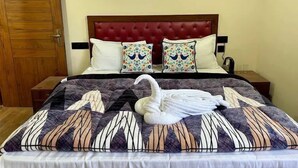 A neatly made bed with a swan towel arrangement, a red upholstered headboard, and two decorative pillows with bird patterns. - Jakhu heights (Shimla)