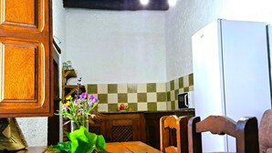 A wooden dining table with a vase of flowers, a microwave, and a refrigerator in a kitchen. - Suitur rural House Cortijo de Don Manuel ( Grandparents) (Granada Algarinejo)
