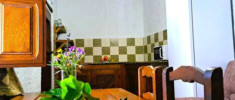 A wooden dining table with a vase of flowers, a microwave, and a refrigerator in a kitchen.