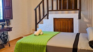 A bedroom with a bed, a green blanket, a wooden staircase, a sewing machine, and a window. - Suitur rural House Cortijo de Don Manuel ( Grandparents) (Granada Algarinejo)