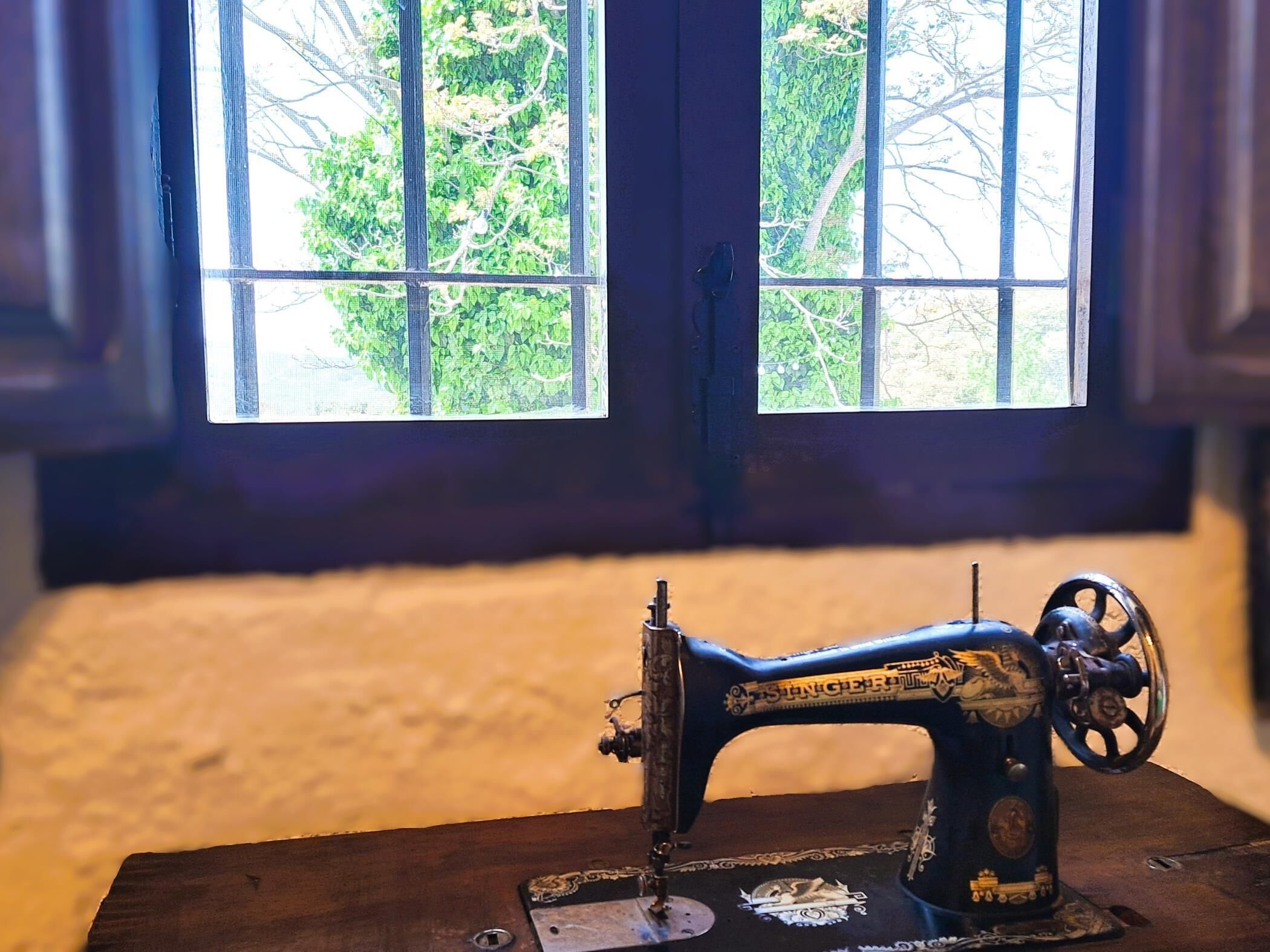 Eine alte Nähmaschine steht auf einem Holztisch, im Hintergrund ein Fenster.