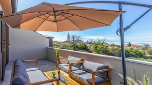 Uma varanda com mesa de madeira, duas cadeiras estofadas, um grande guarda-sol e vista para a paisagem ao redor.