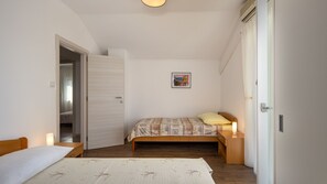 Ein Schlafzimmer mit Bett, Nachttischen, einem Kleiderschrank und einer Tür zu einem weiteren Raum.