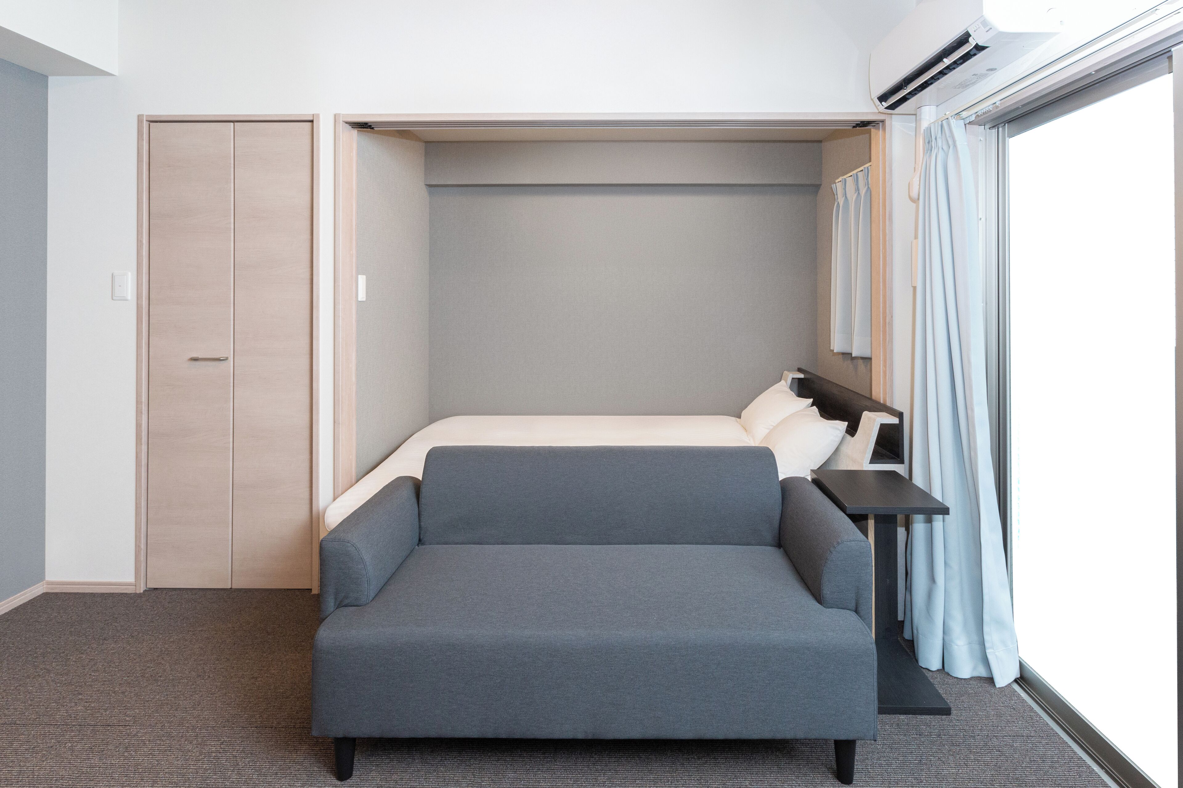 A compact room with a bed, a sofa, a small table, and a wardrobe.
