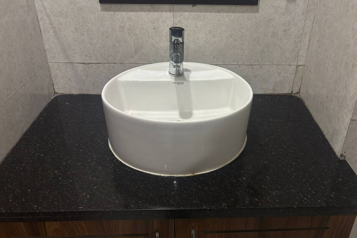 Un baño con un lavamanos blanco sobre una encimera negra, un gabinete de madera debajo y una pared de azulejos.