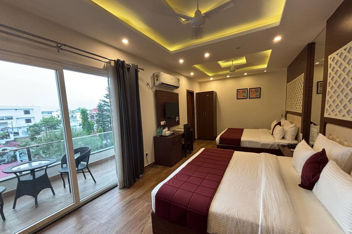 Habitación de hotel con dos camas, un balcón con mesa y sillas, y un ventanal grande.