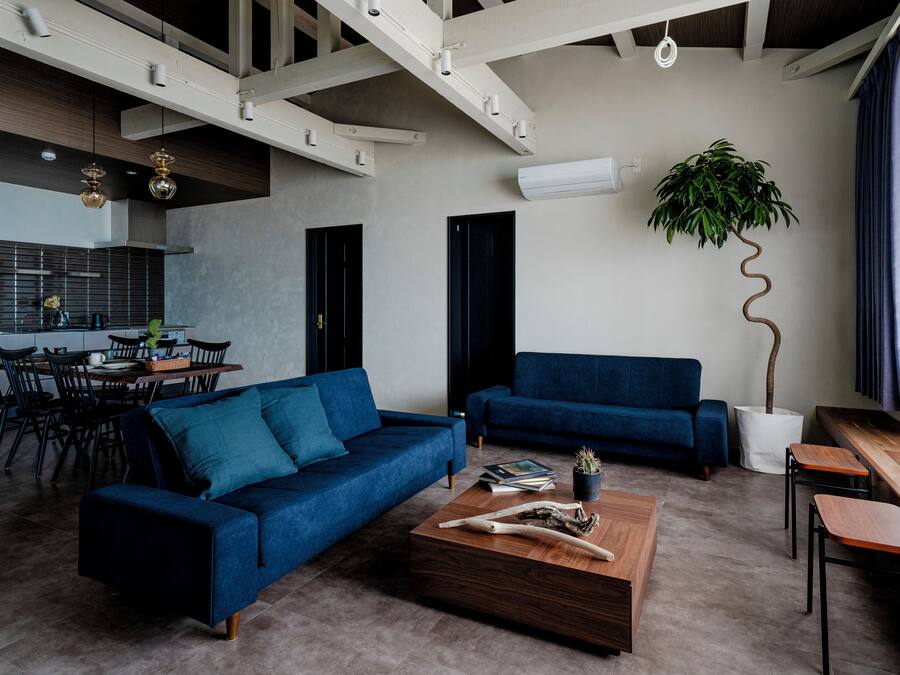 A modern living room with a blue sofa, a wooden coffee table, and a dining area with a table and chairs.