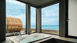 A modern bathroom with a large bathtub, a wooden barrel, and a view of the sea. - UMITOMA OCEAN VIEW RESORT ECHIZEN (Fukui)