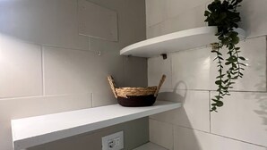 A bathroom with white tiled walls, a white shelf with a woven basket, and a potted plant on a white shelf. - APARTMENT WITH A PRIVATE PATIO NEAR ST. PETER'S (Roma)