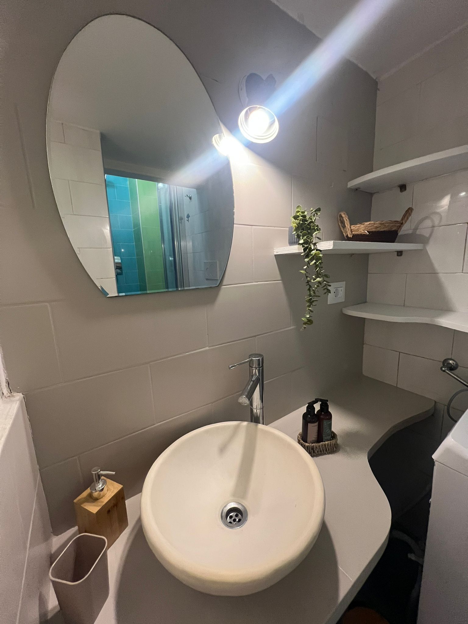 Une salle de bain avec un lavabo rond, un miroir, un porte-serviettes et une étagère contenant des articles de toilette.
