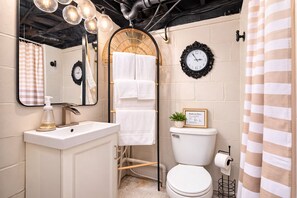 Un baño moderno con un lavamanos blanco, inodoro, zona de ducha y espejo con reloj.