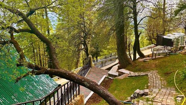 Un camí amb barana metàl·lica, envoltat d'arbres i una estructura amb teulada verda.